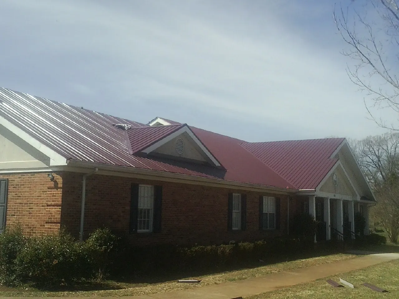 Red metal roof with gabled entries on a long brick building, from a Hail Damage Roof Repair job in Bainbridge Island