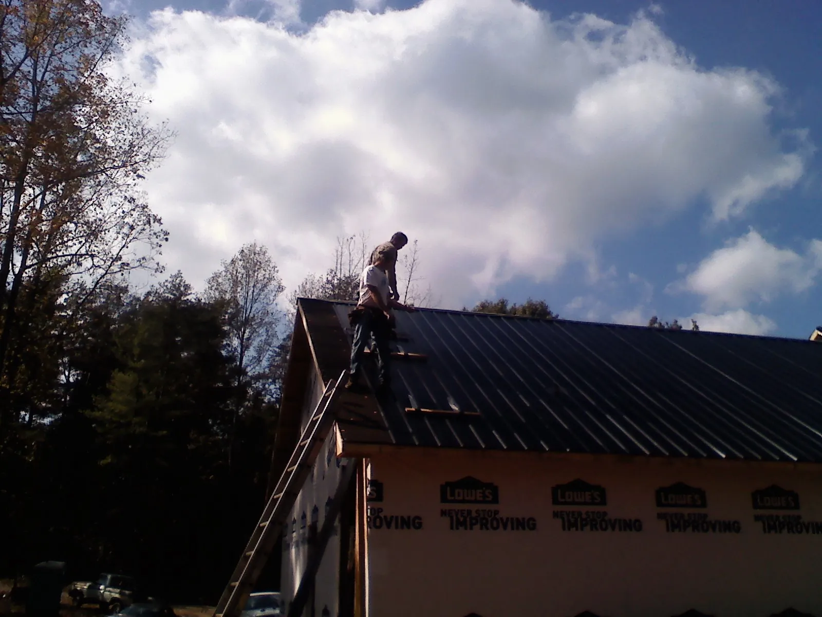 Roofer fastening dark metal panels high against a cloudy sky, from a Roof Inspection job in Bainbridge Island