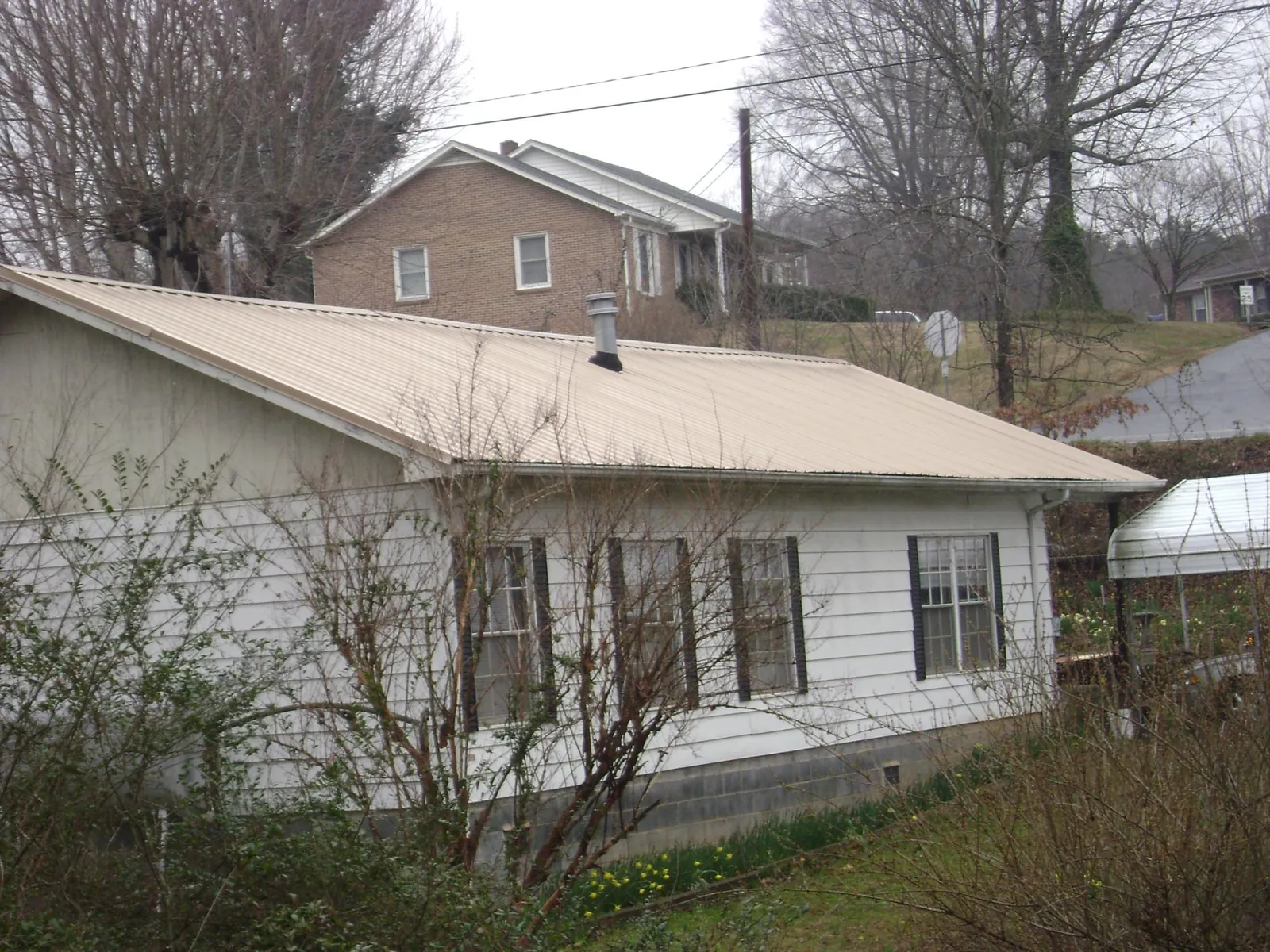 Tan metal roof on a white sided house set into a hillside — Commercial Roofing by Roofing Brothers in Bainbridge Island